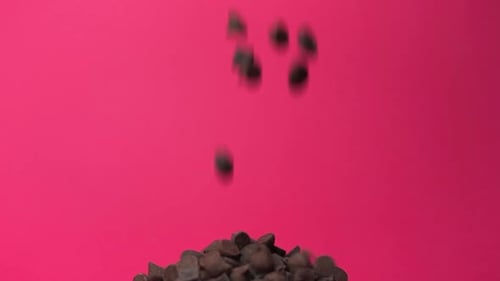Chocolate chips falling onto pile in slow motion with pink background close up macro