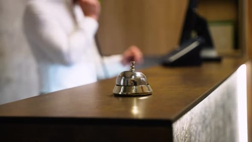 Guest Ringing Service Bell at Front Desk Waiting to Receive Assistance From Hotel Staff at Reception