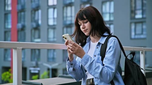 Young Beautiful Smiling Woman with Backpack Using Smartphone Outdoors