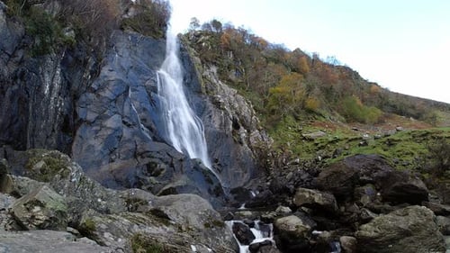 Rocky cascading waterfall flowing into jagged river rocks and boulders low angle time lapse