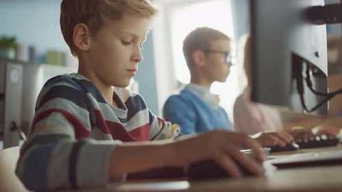 Elementary School Computer Science Classroom: Smart Little Boy Uses Personal Computer, Learning How