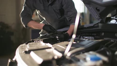 Auto Service Young Man in Uniform with Tool in His Hands Checks Car Engine Near Open Hood at Station