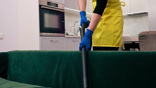 in an Apartment Cleaner in a Yellow Apron Does a Steam Cleaning of a Green Sofa with Professional