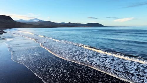 Aerial View of Black Sand Volcanic Beach with Crashing Waves Cinematic Long Drone Shot Serene and
