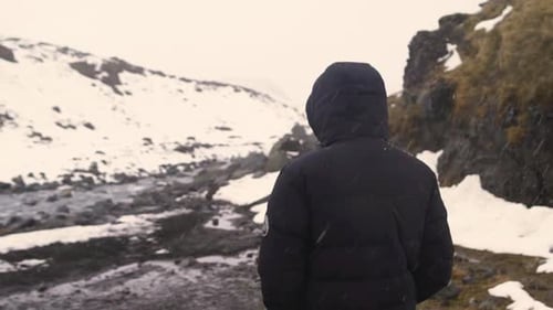 Back View of Young Man in Black Jacket Walking in Winter Mountain