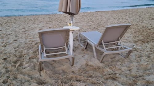 Empty sunbeds and closed umbrella on a sandy beach in the evening on cloudy day