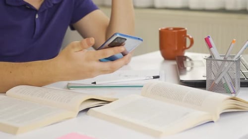 Student Studying with Books, Laptop, and Smartphone