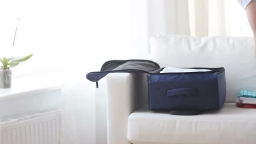 Man Packs Clothes in Luggage at Home on Sofa