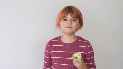 Cute Redhead Girl Child Caucasian Bites a Green Apple Chewing Over White Background Mock Up Copy