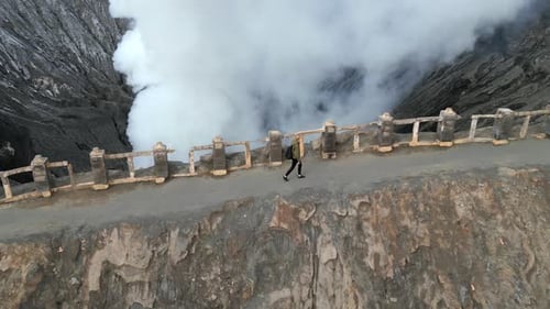 Woman Walking Along the Rim of Steaming Mount Bromo Volcano Crater in Indonesia