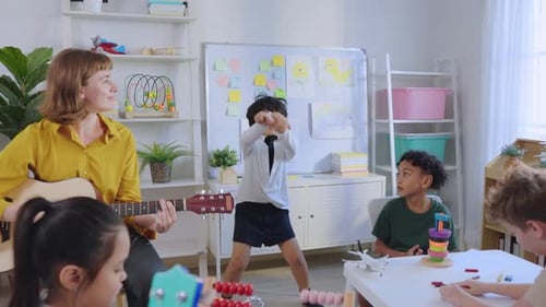Caucasian young woman teacher playing guitar with students in school.