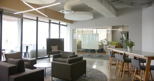 Modern office lounge with comfortable seating, large windows bringing in natural light, copy space