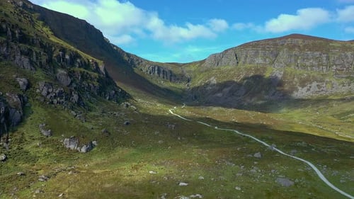 Aerial view of a mountain valley and winding path leading to a waterfall in the South of Ireland dur