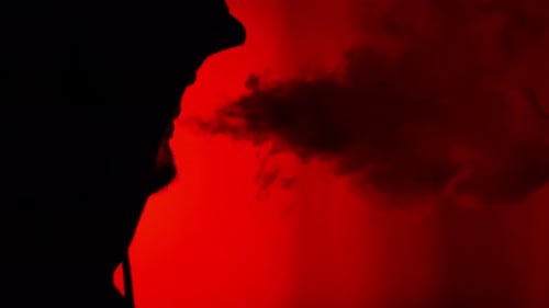 Silhouette smoking or vaping exhaling vapor on red