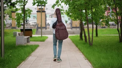 Woman Walks with Guitar Case Solitary Musician Heads Toward Urban Plaza Serene Guitarist Makes Her