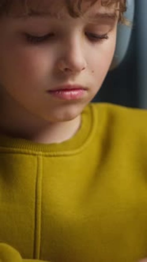 Closeup of a Thoughtful Young Boy with Curly Hair Wearing a Mustard Yellow Sweater Focusing on His