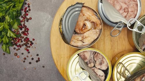 Opening Metal Cans with Canned Fish and Pate on Table Rotating on Wooden Desk Top View Canned Salmon