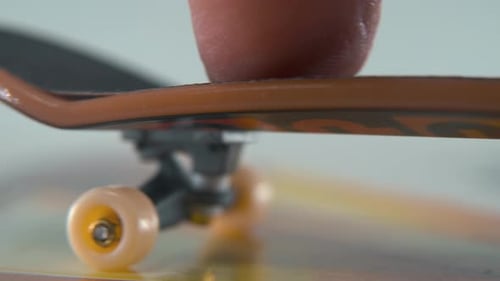 A hyper close-up detailed shot of a mini skateboard, tiny white wheels, riding fingerboard from righ