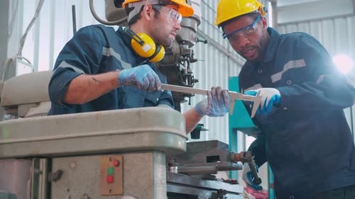 Two young engineer man examining and measuring steel together with expertise at lathe factory.