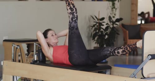 Fit senior caucasian woman stretching on reformer in pilates studio, unaltered, in slow motion