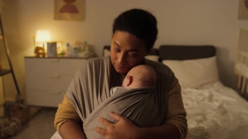 Mother Cradling Sleeping Baby at Night Indoors