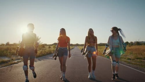 Women Skaters in Summer Clothes and Protective Gear Walk on Road