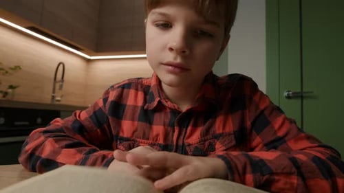 Focused Boy Reading a Book in Kitchen