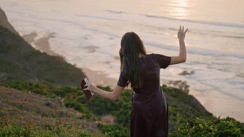 Niña camina por la costa agreste hasta el océano con un libro al atardecer