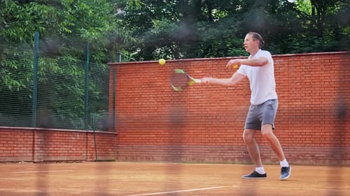 Young Attractive Man Playing Tennis on Orange Clay Tennis Court