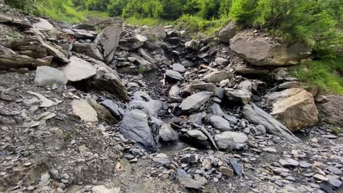 Tiny mountain stream flowing calmly on rough rocks, boulders and pebbles, close-up