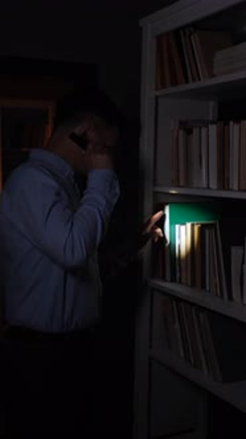 Vertical Video Man Searching for Book on Bookshelf Using Flashlight in Dark Room