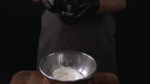 Males hands break egg into the flour, close-up.
