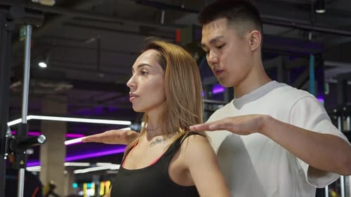 A Fitness Trainer Watches His Client Perform Shoulder Exercises in Front of a Gym Mirror