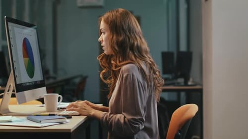 Excited business woman enjoys project results on computer screen late at night office
