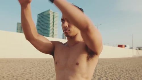 Young athletic man standing on the beach stretching his arm muscles before training