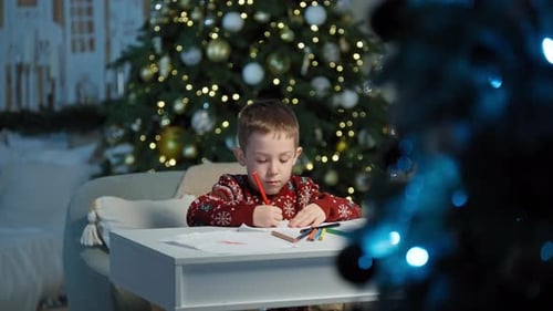 Boy Drawing Christmas Pictures at Table by Christmas Tree