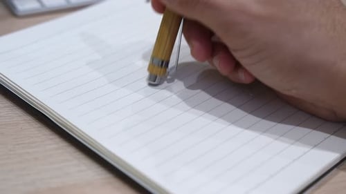 Hand Holding Bamboo Pen Over Blank Notebook