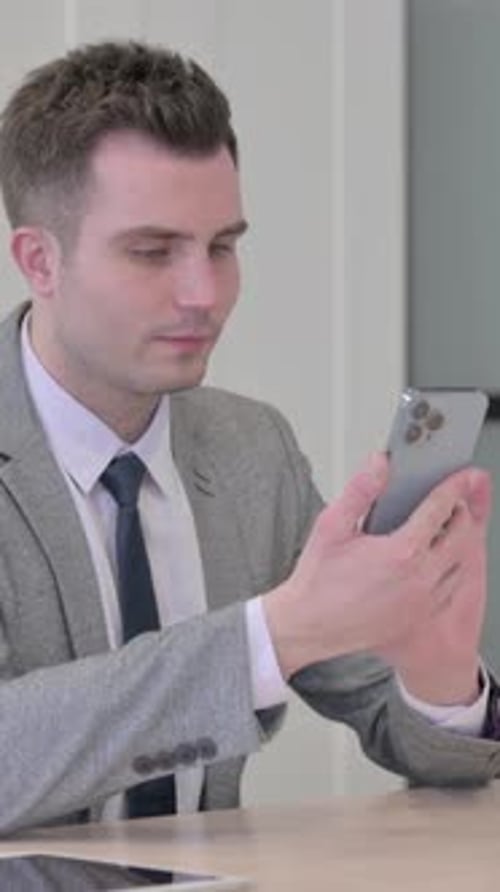 Young Businessman Browsing Internet on Smartphone in Office, vertical video