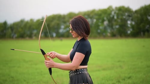 Woman Shoots Arrow in Field Female Bowman Aligns Arrow in Countryside Setting Young Woman Expertly