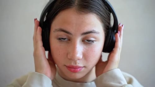 Junge Frau mit Kopfhörern blickt lächelnd in die Kamera, hört Musik, Radio, Podcast, Tanz, genießt das Leben