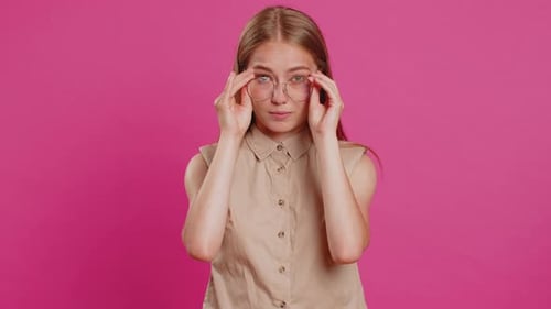 Woman Puts on Glasses in Front of Pink Background