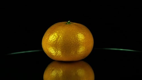 Vue en angle réduit : l'orange clémentine tourne sur un miroir dans un studio sombre