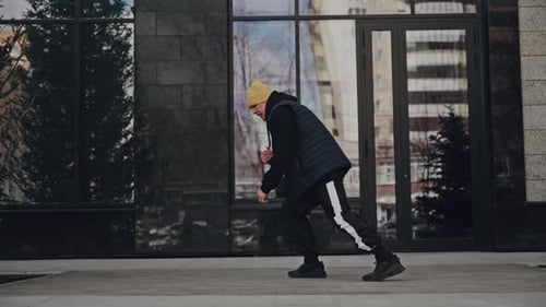 Man in Black Jacket and Yellow Beanie Walking Confidently on a City Sidewalk