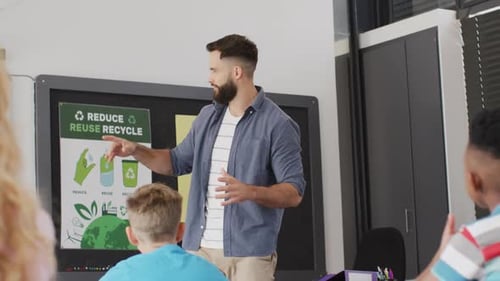 Diverse male teacher and happy schoolchildren at desk in school classroom