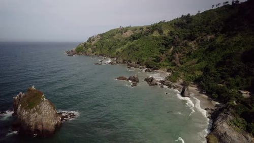 Rocky coastline with cliffs and waves crashing on a tropical beach at sunset