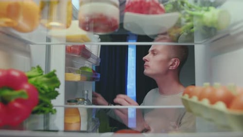 Young Adult Reaching into Full Refrigerator at Night