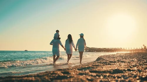 Happy Family Mom Daughter Dad Son Walking Together on Sea Beach in Summer Day Rear View
