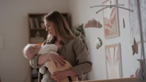 Woman Holds Baby in Nursery Near Crib
