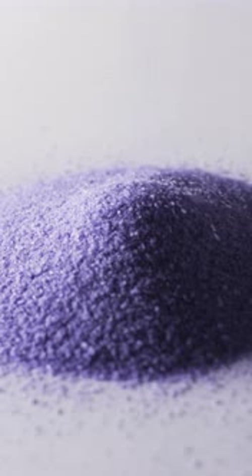 Vertical video of close up of heap of purple sand grains and copy space on white background
