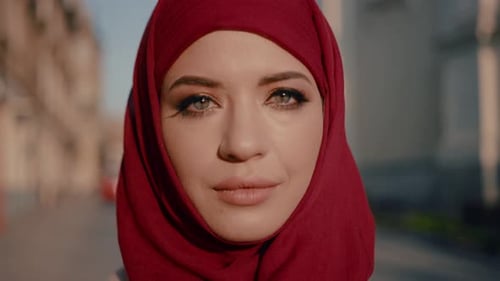 Wunderschöne muslimische junge Frau im roten Hijab schaut und lächelt in die Kamera auf wunderschönem Hintergrund
